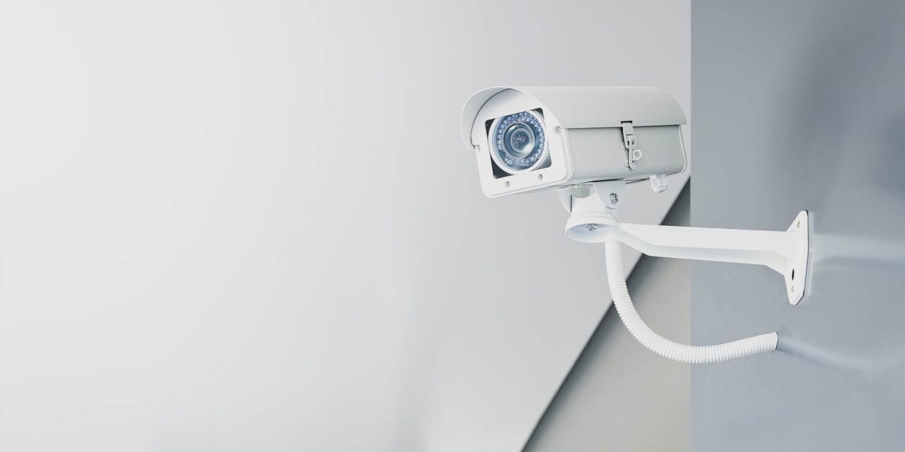 Illustrative photograph of a white CCTV camera mounted on a wall
