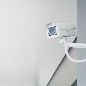 Illustrative photograph of a white CCTV camera mounted on a wall