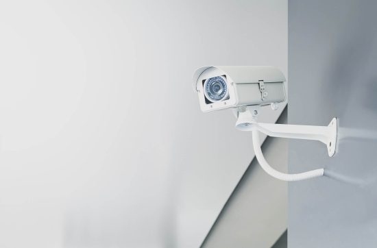 Illustrative photograph of a white CCTV camera mounted on a wall