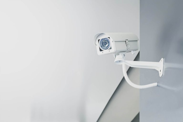 Illustrative photograph of a white CCTV camera mounted on a wall